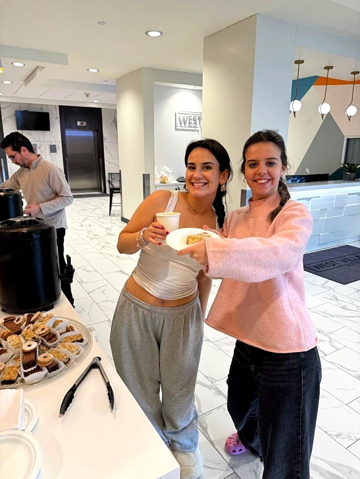 Two residents smiling with coffee and pastries at the West Village Suites coffee social